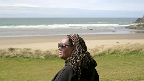 Beautiful-modern-black-woman-on-beach,-looking-out-on-to-the-ocean,-laughing