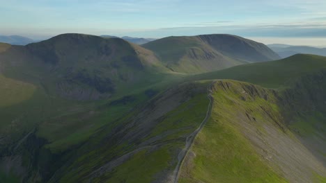 Flying-above-mountain-path-towards-ancient-glaciated-mountains-and-fells-during-golden-hour