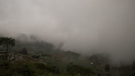 Swirling-clouds-on-moody-dark-agricultural-hillside-landscape,-Dieng-plateau,-Indonesia