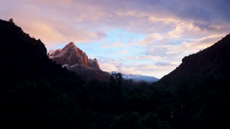 Zion-National-parks-mountain-range-with-snow,-during-sunset-casting-light-onto-the-mountains-in-the-background