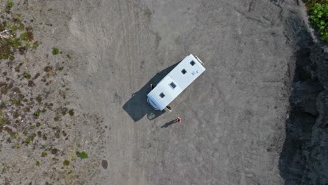 Birds-eye-drone-shot-of-a-man-standing-in-front-of-a-RV,-parked-in-a-sand-pit