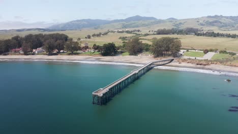 Toma-Aérea-Descendente-Y-Panorámica-Del-Muelle-De-La-Playa-Conmemorativa-De-William-Randolph-Hearst-En-El-Antiguo-Pueblo-De-San-Simeón-En-La-Costa-Central-De-California