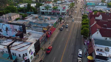 Toma-Aérea-Sobre-La-Avenida-Melrose,-Automóviles-Circulando-En-El-Popular-Distrito-Comercial-De-Los-Ángeles-Durante-El-Día