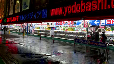 Noche-Lluviosa-En-Tokio-Con-Gente-Caminando-Frente-A-Una-Tienda-Brillantemente-Iluminada