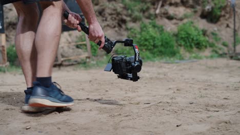 Male-hold-camera-equipment-on-gimbal-stabilizer-and-walk-on-sandy-ground