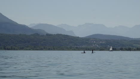 Menschen-Paddeln-Auf-Einem-Alpensee-In-Frankreich-Mit-Reflektiertem-Wasser-Und-Bergen-Im-Hintergrund