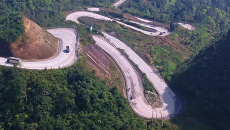 This-drone-footage-captures-the-winding-mountain-roads-of-Ha-Giang-in-North-Vietnam,-featuring-vehicles-navigating-the-sharp-curves-and-dramatic-elevation-changes