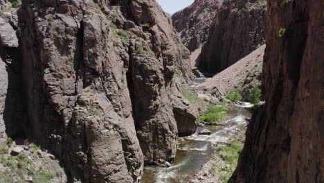 Un-Dron-Captura-Una-Vista-Impresionante-De-Los-Imponentes-Acantilados-Que-Rodean-Un-Sereno-Desfiladero-De-Un-Río,-Bañados-Por-El-Resplandor-De-La-Luz-Del-Sol-Del-Mediodía.