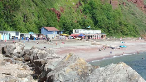 People-enjoying-the-sun-playing-on-beach-and-swimming-in-sea-on-Oddicombe-beach-on-holiday-in-Babbacombe,-Torquay,-Devon,-England-UK