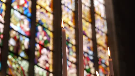 Candles-burning-in-front-of-stained-glass-windows-in-a-church