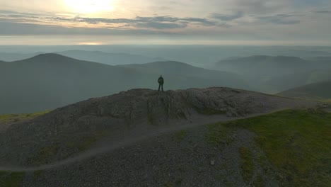 Bergwanderer-Einsame-Gestalt-Auf-Dem-Berggipfel-Mit-Umlaufbahn,-Die-Zur-Goldenen-Stunde-Neblige-Täler-Und-Abgerundete-Berggipfel-Enthüllt