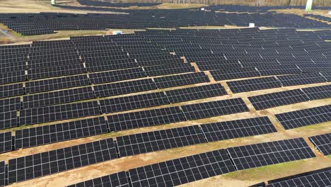 Drone-shot-of-large-power-plant-of-solar-panels-and-wind-turbine-in-a-vast-field-on-a-sunny-day-in-Taurage,-Lithuania