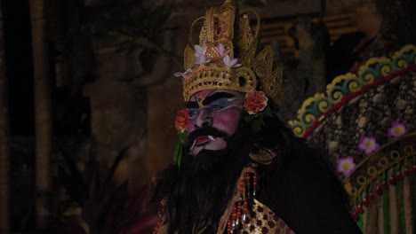 A-performer-in-elaborate-traditional-Balinese-attire-is-captured-in-a-close-up-shot,-showcasing-intricate-face-paint,-a-majestic-headdress-adorned-with-flowers,-and-vibrant-costume-details