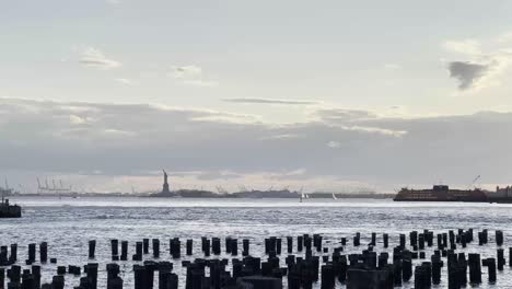 Statue-of-Liberty-seen-from-the-waterfront,-with-the-calm-waters-and-wooden-pilings-in-the-foreground