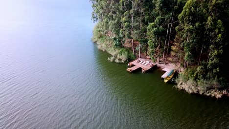 Sonnenliegen-Auf-Holzsteg-Mit-Touristen,-Die-Im-Bunyonyi-See,-Uganda,-Schwimmen