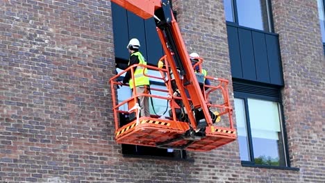 Eine-Statische-4K-Aufnahme-Von-Arbeitern,-Die-Auf-Einer-Hubarbeitsbühne-Die-Fenster-Eines-Neuen-Gebäudes-Putzen