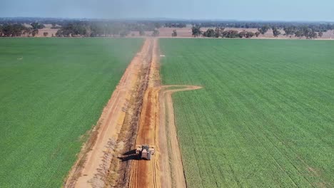 Grader-being-towed-by-a-large-tractor-along-the-dirt-road-of-a-farm