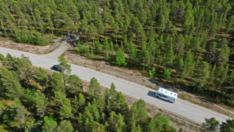 Vista-Aérea-De-Seguimiento-De-Una-Autocaravana-Conduciendo-Por-Un-Camino-Forestal-De-Abetos,-Verano-En-Finlandia