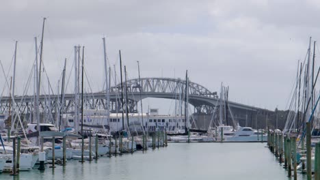 Ocean-Water-Westhaven,-Veleros-Estacionados-Cerca-De-Los-Postes-Y-El-Puente-Del-Puerto-En-El-Fondo-En-Auckland,-Suiza