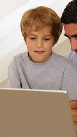 Niño-Usando-Una-Computadora-Portátil-Con-Su-Padre-En-La-Mesa