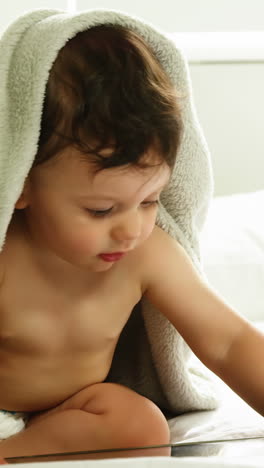 Cute-baby-with-blanket-on-head-playing-with-tablet-