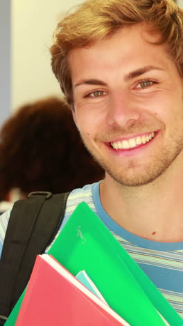 Handsome-student-leaning-on-locker-smiling-at-camera