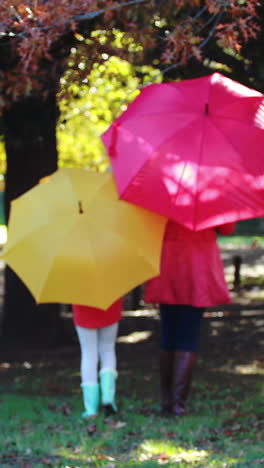 Mother-and-daughter-walking-together-in-park-under-umbrella