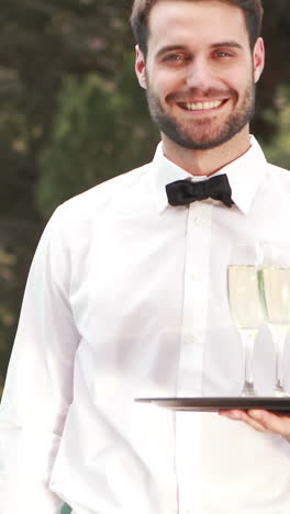 Smiling-waiter-holding-champagne-glasses