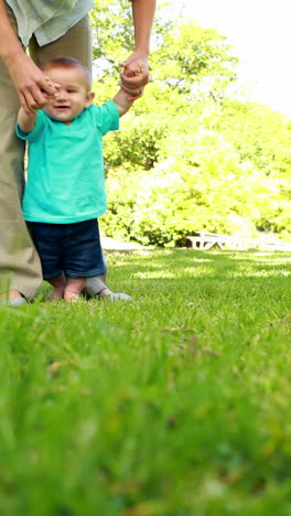 Mother-helping-baby-son-to-walk-on-the-grass