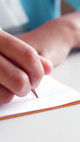 Mid-section-of-school-kid-doing-homework-in-classroom-at-school