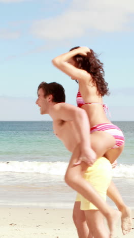 Man-giving-his-girlfriend-a-piggy-back-at-the-beach