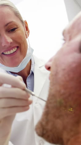 Female-dentist-examining-male-patient-with-dental-tools