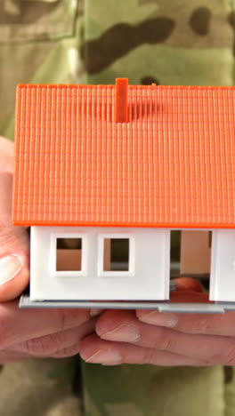 Mid-section-of-soldier-holding-house-model-on-white-background