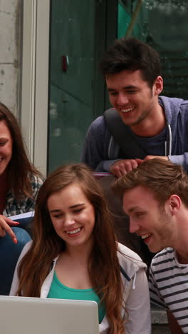 Cheerful-friends-using-laptop-on-stairs