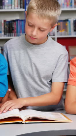 Niños-De-La-Escuela-Leyendo-Un-Libro-Juntos-En-La-Biblioteca