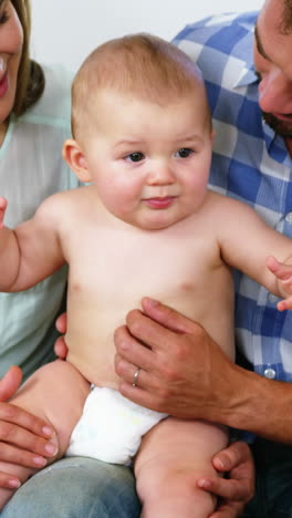 Glückliche-Eltern-Sitzen-Und-Halten-Ihr-Baby-Auf-Dem-Sofa