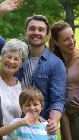 Multi-generation-family-smiling-and-waving-at-camera-in-a-park