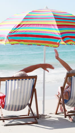 Retired-old-couple-lying-on-deckchair-while-doing-high-five