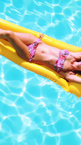 Overhead-of-brunette-lying-on-lilo-in-pool-on-sunny-day