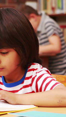 Pupil-reading-book-at-desk-in-library