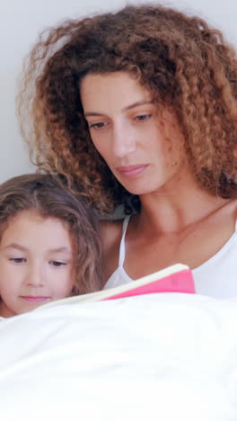 Focused-mother-reading-book-to-her-daughter