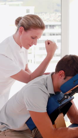 -Terapeuta-Femenina-Masajeando-A-Un-Hombre-Sentado-En-Una-Silla-De-Masaje