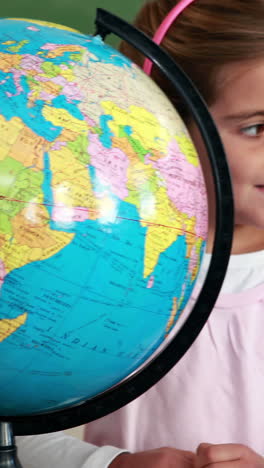 Cute-pupils-smiling-around-a-globe-in-classroom