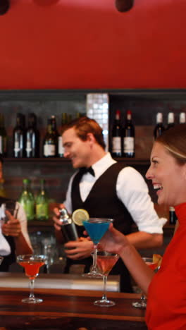 Two-women-with-cocktail-drinks-talking-to-each-other-at-counter