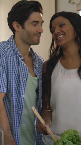 Man-kissing-a-woman-while-mixing-a-salad-in-kitchen