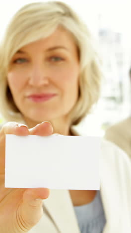 Smiling-businesswoman-showing-her-card-with-team-behind-her