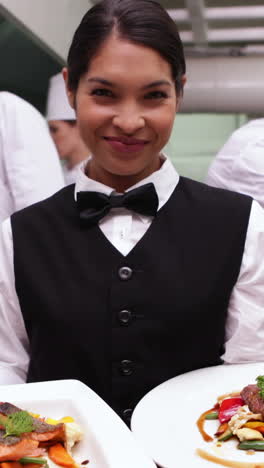 Smiling-waitress-showing-two-dishes-to-camera