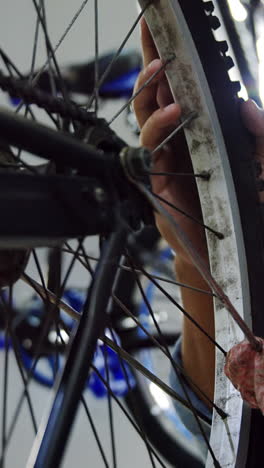 Mechanic-cleaning-bicycle-spoke-in-workshop