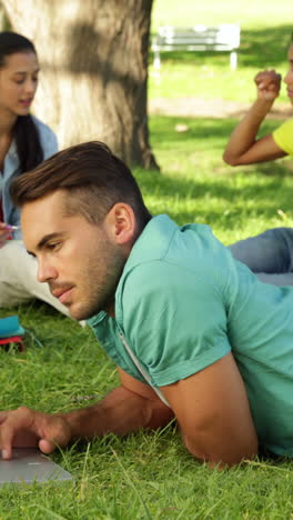 Smiling-student-using-his-laptop-in-front-of-his-friends