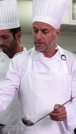 Chef-showing-colleague-content-of-pot-and-smiling-at-camera